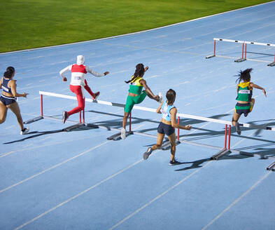 Female track and field athletes jumping hurdles in competition - CAIF31486