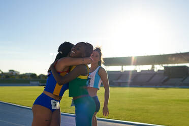 Weibliche Leichtathleten umarmen sich auf einer sonnigen Bahn - CAIF31507
