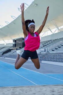 Female track and field athlete long jumping over sand - CAIF31520