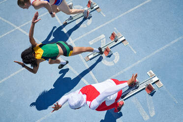 Female track and field athletes taking off from starting blocks - CAIF31542