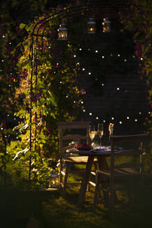 Champagner und rote Johannisbeeren auf einem idyllischen Gartentisch bei Sonnenuntergang - CAIF31573