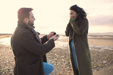 Mann macht seiner Freundin am sonnigen Winterstrand einen Heiratsantrag - CAIF31579