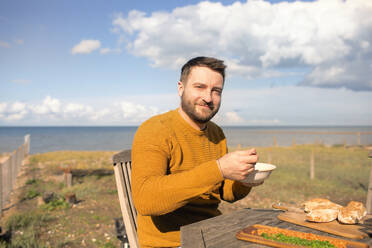 Portrait happy man eating on sunny ocean beach patio - CAIF31583