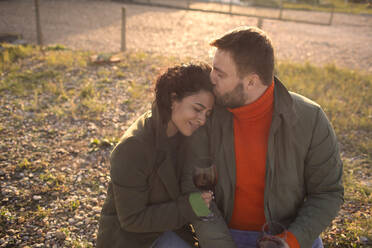 Glückliches, zärtliches Paar trinkt Wein auf einer sonnigen Terrasse - CAIF31600