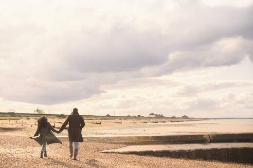 Couple holding hands walking on sunny tranquil winter beach - CAIF31604