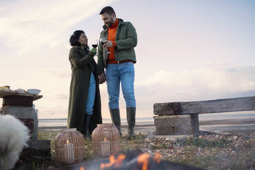 Pärchen in Wintermänteln genießt Rotwein am Strand - CAIF31620