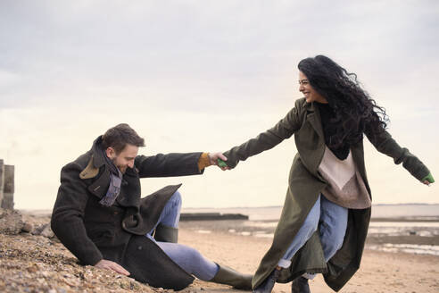 Verspieltes Paar in Wintermänteln am Strand - CAIF31625