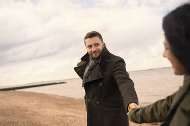 Couple in winter coats holding hands on ocean beach - CAIF31627