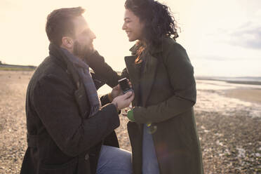 Boyfriend with wedding ring proposing to girlfriend on winter beach - CAIF31629