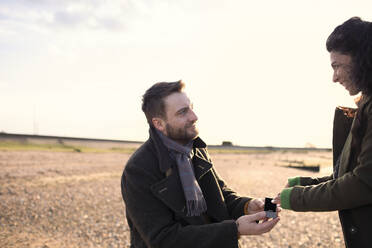 Man proposing to girlfriend on sunny winter beach - CAIF31637