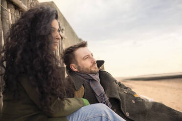 Serene couple in winter coat relaxing on beach - CAIF31650