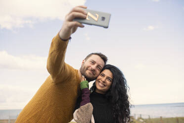 Happy couple taking selfie on ocean beach - CAIF31652