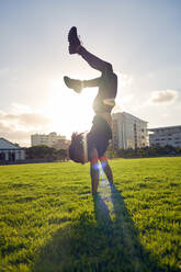 Unbekümmerter junger Mann macht Handstand im sonnigen Parkgras - CAIF31681