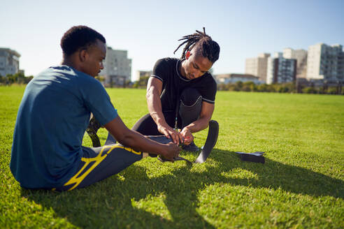 Coach helping young male amputee athlete with running blade prosthetic - CAIF31696