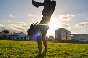 Athletic young man doing handstand in sunny park grass - CAIF31701