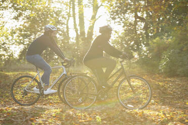 Couple bike riding through autumn leaves in sunny park - CAIF31708