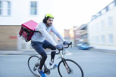 Männlicher Fahrradkurier, der in einem städtischen Viertel Lebensmittel mit dem Fahrrad ausliefert - CAIF31709