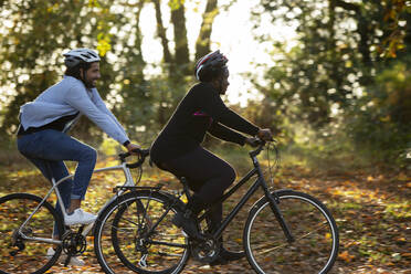 Friends riding bicycles through autumn leaves in park - CAIF31710