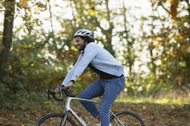 Glücklicher junger Mann auf dem Fahrrad im Herbstpark - CAIF31721