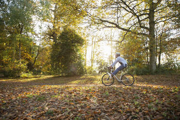 Unbekümmerte junge Frau fährt mit dem Fahrrad durch Herbstlaub im Park - CAIF31722