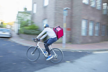 Männlicher Fahrradkurier, der auf einer städtischen Straße Lebensmittel ausliefert - CAIF31730