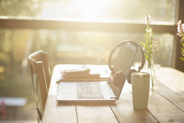 Kopfhörer, Laptop und Kaffee auf einem sonnigen Tisch im Café - CAIF31734