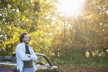 Happy man at convertible in sunny autumn park - CAIF31735