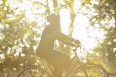Frau mit Helm auf dem Fahrrad in einem sonnigen Herbstpark - CAIF31736