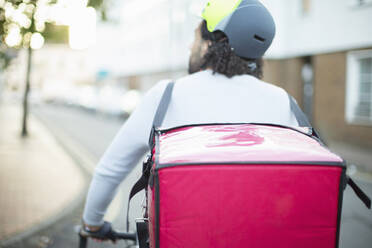 Männlicher Fahrradkurier mit Helm, der auf einer städtischen Straße Lebensmittel ausliefert - CAIF31738