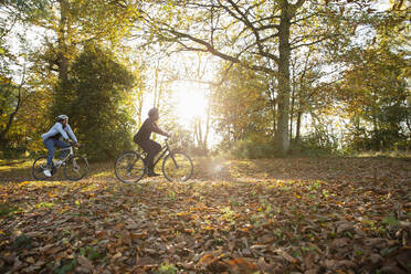Couple riding bicycles in autumn leaves in sunny sunny park - CAIF31739