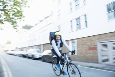Männlicher Fahrradkurier, der auf einer städtischen Straße Lebensmittel ausliefert - CAIF31740