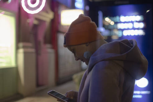 Stilvolle Frau, die nachts ihr Smartphone auf dem Bürgersteig benutzt - CAIF31771