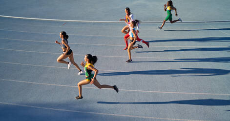 Female track and field athletes running in competition on blue track - CAIF31777