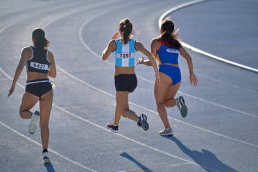 Female track and field athletes running on sunny track stock photo