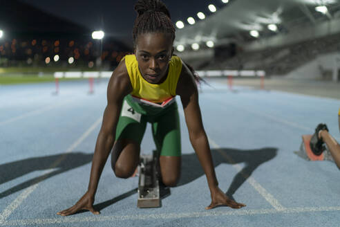 Portrait determined female track and field runner at starting block - CAIF31786