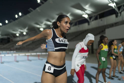 Focused female track and field athlete stretching before race on track - CAIF31790