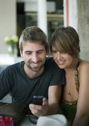Männliche und weibliche Freunde teilen sich ein Mobiltelefon im Restaurant - AJOF01517