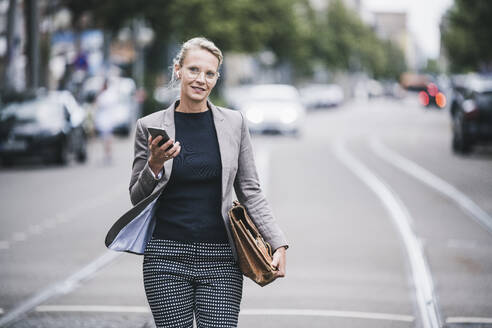 Weibliche Fachkraft hält Handy und Tasche beim Gehen in der Straßenbahn - UUF23908