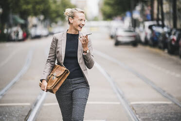 Happy female professional talking on mobile phone while walking at tramway - UUF23911