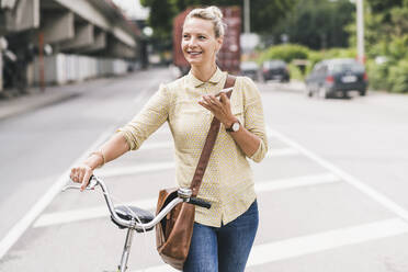 Female professional talking on mobile phone while wheeling bicycle - UUF23928