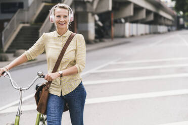 Glückliche weibliche Fachkraft hört Musik über Kopfhörer, während sie Fahrrad fährt - UUF23932
