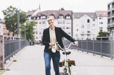 Lächelnde weibliche Fachkraft mit Kopfhörern, die auf einer Brücke Fahrrad fährt - UUF23934