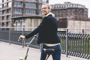 Glückliche Frau zu Fuß mit Fahrrad auf einer Brücke - UUF23940