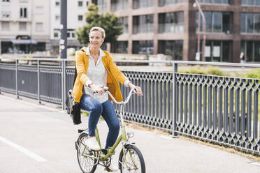 Businesswoman with shoulder bag riding bicycle on bridge - UUF23948