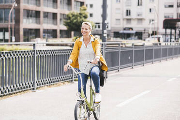 Weibliche Fachkraft lächelt beim Fahrradfahren auf einer Brücke - UUF23949