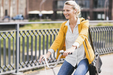 Lächelnder weiblicher Pendler mit Umhängetasche auf dem Fahrrad - UUF23950