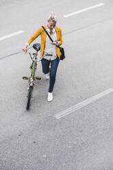 Berufstätige Frau, die ein Mobiltelefon benutzt, während sie mit dem Fahrrad auf der Straße geht - UUF23953