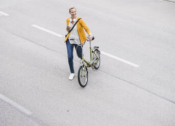 Smiling female professional walking with bicycle on street - UUF23956