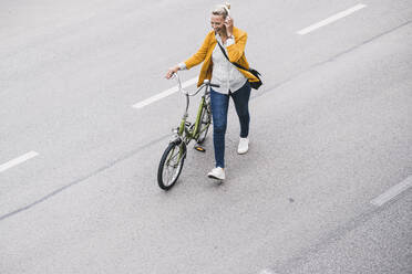 Weiblicher Pendler hört Musik über Kopfhörer, während er mit dem Fahrrad auf der Straße fährt - UUF23957