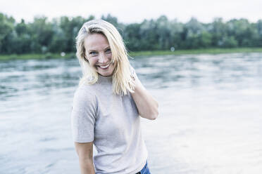 Blonde Frau lächelt, während sie am Fluss steht - UUF23978